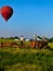 A young Amish man cuts grass in the field, with a hot air balloon hovering above