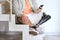 Young amputee man with leg prosthesis sitting on stairs at home using phone.