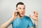 Young angry caucasian guy in blue t-shirt talk and scream on the phone, on light gray background
