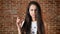 Young angry girl clenching her fist and looking into the camera, threatening, brick wall in the background, portrait