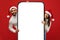 Young arab couple in Santa hats standing near big phone with empty screen advertising application or Christmas offer