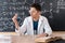 A young Arab male chemistry teacher sits at a table against the background of a chalk board with different formulas