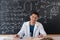 A young Arab male chemistry teacher sits at a table against the background of a chalk board with different formulas