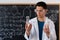 A young Arab male chemistry teacher stands against the background of a chalk board with different formulas, dressed in a