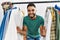 Young arab man customer smiling confident appearing through clothes rack at clothing store