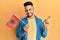 Young arab man holding albania flag smiling happy pointing with hand and finger to the side