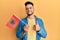 Young arab man holding albania flag smiling happy and positive, thumb up doing excellent and approval sign