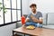 Young arab man smiling confident eating fried chicken drinking soda beverage at home