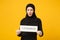 Young arabian muslim woman in hijab black clothes hold in hands sign with censored title isolated on yellow wall