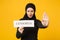 Young arabian muslim woman in hijab black clothes hold in hands sign with censored title isolated on yellow wall