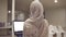 Young arabic female wearing a hijab going by the hall while holding her black laptop in hands. Employee, working place