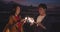 Young asia couple having fun and celebrates with sparklers lights in camping on beach at night. Male and female traveler relax at