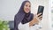 Young Asia muslim businesswoman using smart phone talk to friend by videochat brainstorm online meeting while remotely work from