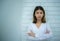 Young asian business woman stands proudly and confidently in front of a white brick background radiating positivity.