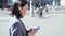 Young Asian business woman wearing suit holding phone walking in big city.