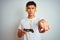 Young asian chinese gamer man playing video game standing over isolated white background pointing with finger to the camera and to