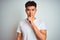 Young asian chinese man wearing t-shirt standing over isolated white background asking to be quiet with finger on lips