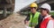 Young Asian civil engineers wearing safety jackets and helmets stand on an under-construction expressway, holding a blueprint of