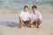 Young asian couple gay smiling romantic drawing heart shape together on sand in vacation