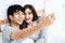 Young asian couple lying on bed and taking selfie by smartphone. Asian lovers take a photo with toothy smile. Happy lover hug each