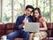 Young Asian couple sitting close together on couch in living room shopping online, a man holding credit card while woman typing