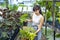 Young Asian customer is choosing exotic plant from the local garden center nursery with shopping cart full of summer plant for