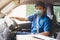 Young asian delivery man wearing protective face mask driving his van with packages on the front seat due to Coronavirus disease