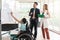 young asian disabled working woman sitting in wheelchair presenting her job with her colleagues in the working place, office room