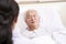 Young asian doctor talking to senior patient at bedside in hospital ward