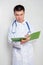 A young Asian doctor in a white coat, with a stethoscope on his neck, holds a green folder in his hands and takes notes.