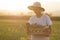 Young asian farmer using mobile phone to contact his customer while carrying a basket of fresh vegetable