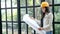 Young Asian female construction engineer in a yellow hard safety helmet hat holding architect blueprints in hand, reading
