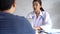 Young Asian female doctor talking to patient at hospital. Physician using laptop and giving diagnosis in doctor`s office