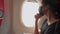 Young Asian Female passenger sitting at window seat on the plane, ticket boarding pass, covid-19 new normal travel keep social dis