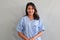 Young Asian female patient in blue hospital patient gown smiling and looking at camera on grey background, authentic half body