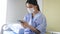 Young Asian female patient sitting on hospital bed wearing surgical face mask for safety using smartphone to text and