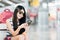 Young Asian girl using smartphone, waiting for flight at airport, sitting on baggage trolley or luggage cart