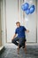 A young Asian handsome man in casual blue shirt was smiling while holding a blue and white balloon and seating on high chair