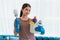 Young Asian housewife wearing gloves and holding basket with cleaners and brushes, cleaning and washing concept