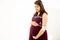 Young asian indian pregnant woman looking at belly standing against white background outdoor studio shot, happy female expecting