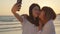 Young Asian lesbian couple using smartphone taking selfie near beach. Beautiful women lgbt couple happy relax enjoy love moment