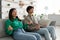 Young Asian male and female meditating with closed eyes, practicing yoga, relaxing on couch in living room, copy space