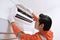 Young asian male technician repairing air conditioner with