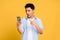 Young Asian man in casual clothes is shocked by something on his smartphone. Yellow background isolated