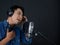 Young asian man with headphone  singing in front of black soundproofing wall. Musician producing music in professional recording