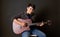 Young asian man with headphones playing an acoustic guitar in front of black soundproofing wall. Musician producing music in