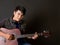 Young asian man with headphones playing an acoustic guitar in front of black soundproofing walls. Musicians producing music in