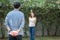 Young asian man holding behind back gift box surprise girlfriend excited in the garden with happy, anniversary day of couple