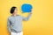 Young Asian man holding blue speech bubble over yellow background