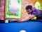 Young Asian man play billiards in the colorful club - Aiming white ball to shot